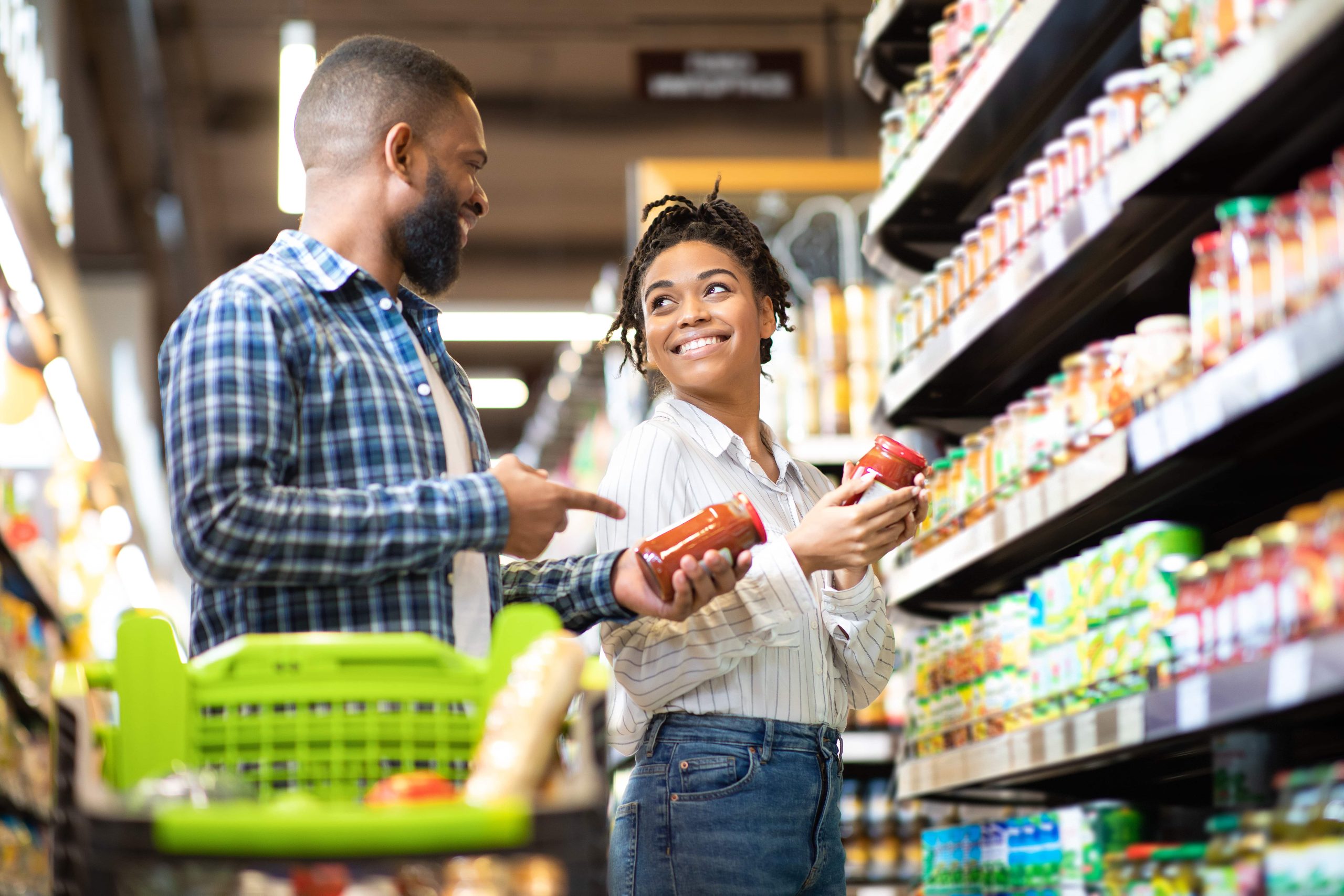 A couple smiling while comparing products in a grocery store aisle, representing modern consumer decision-making and shopping behavior